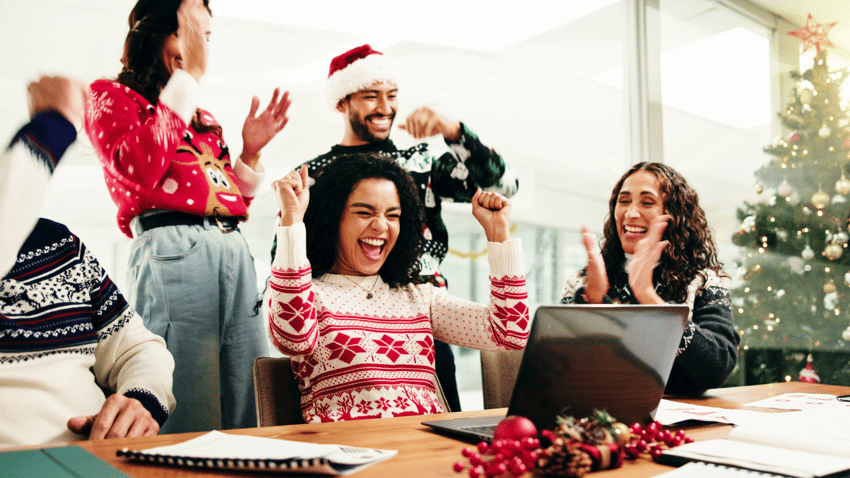 Team in Weihnachtspullis freuen sich am Arbeitsplatz