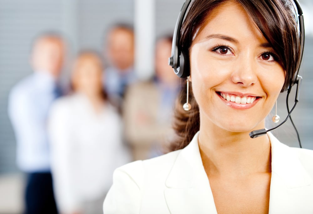Lächelnde Support-Mitarbeiterin mit Headset im Hintergrund mehrere verschwommene Personen